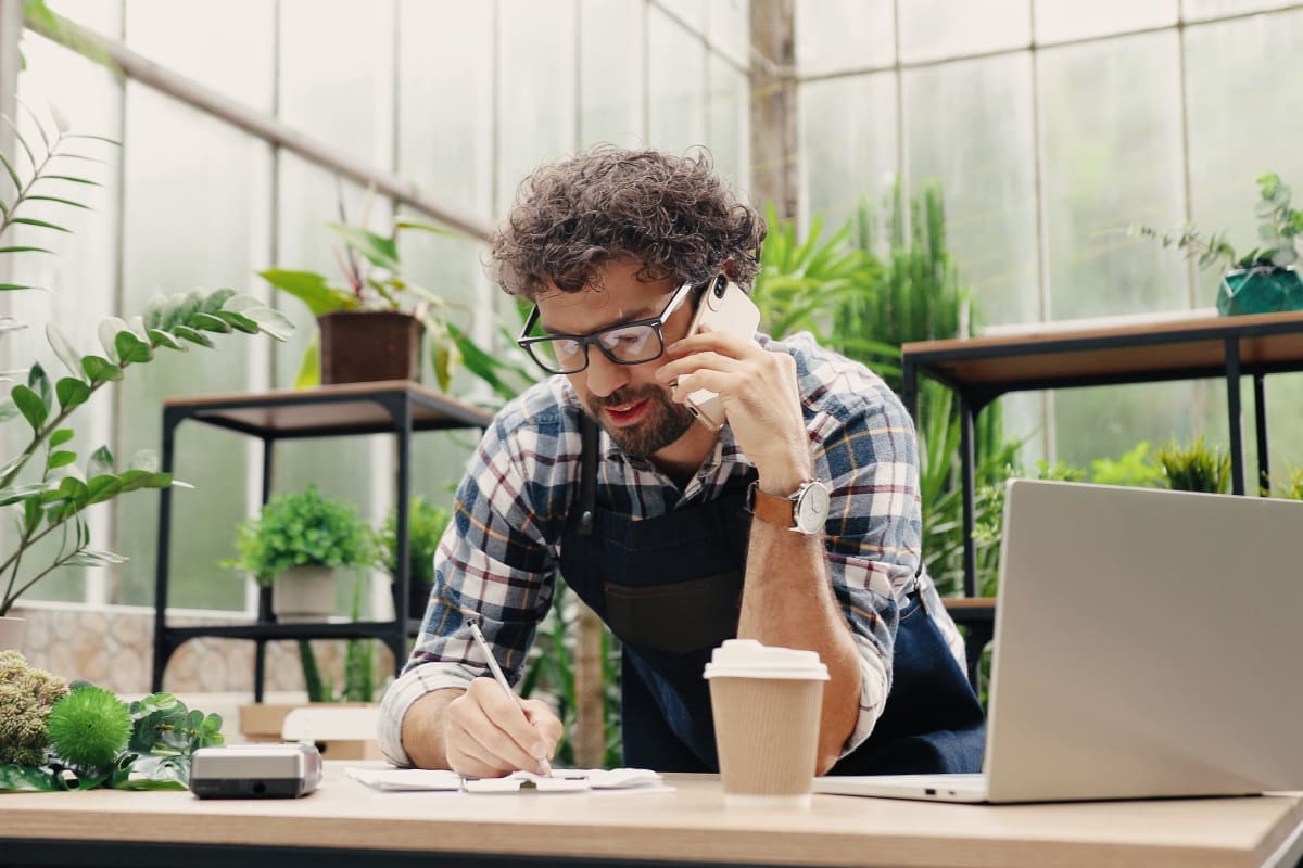 man in greenhouse on phone writing